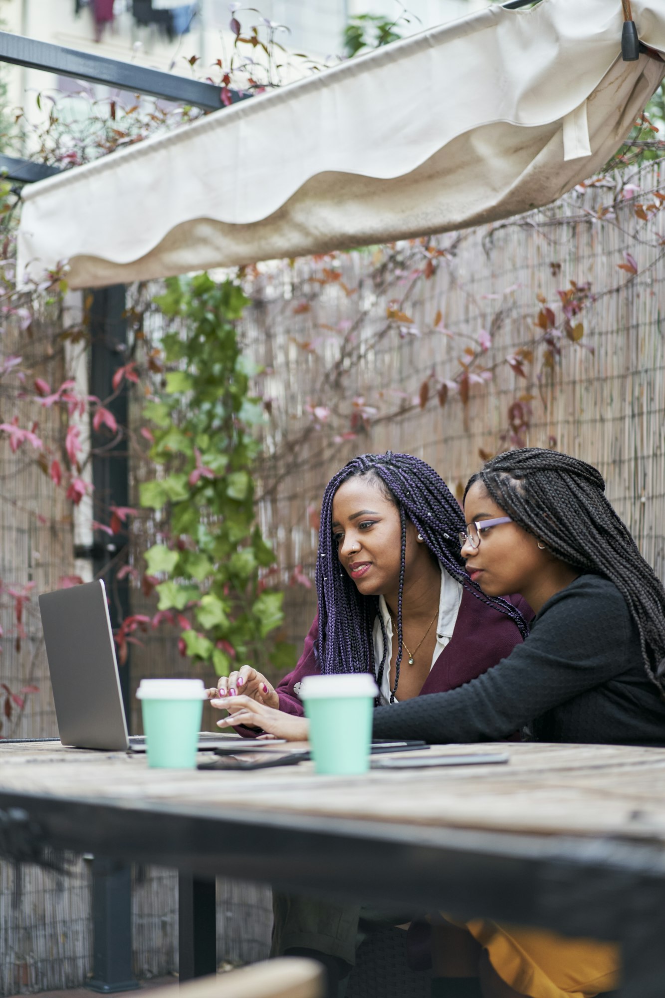 Vertical shot of two young latin women using a laptop outdoors.